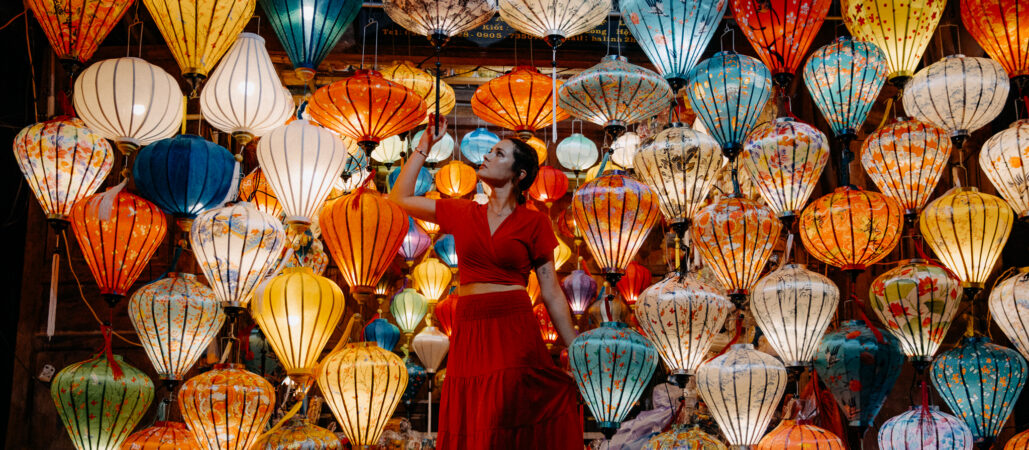 Žena v červených šatech před stěnou rozsvícených lampionů ve Vietnamu