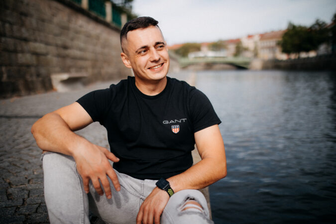 Muž v černém tričku sedí na kamenném nábřeží u řeky
